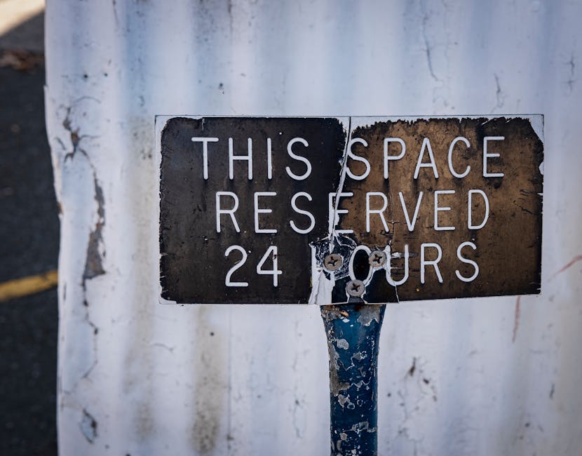 A weathered metal sign attached to a blue pole indicating a reserved space available 24 hours a day. The sign's surface shows rust, peeling paint, and faded black paint with white uppercase lettering stating 'THIS SPACE RESERVED 24 HOURS.' The signs are secured to the pole with screws, some of which are rusted, and the background features a white wall with visible cracks and peeling paint. The environment suggests an outdoor urban setting, possibly a parking area or designated space for specific use, aligning with the context of private or alternative waste management and rubbish removal services like those offered by Rubbish Collection Islington.